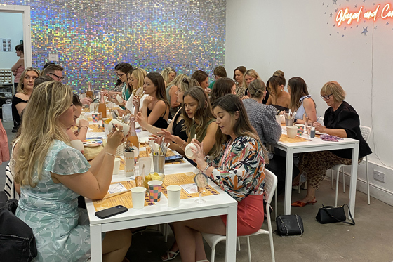 Group pottery painting at long tables with glittery wall in background